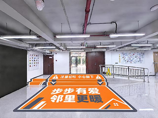 重新设计地贴，现代简约风格：1. 最上层台阶的"注意台阶 小心脚下"文字完全倒置（从进门方向看是正向可读的，从当前拍摄视角看文字是倒过来的），确保进门下台阶的人正读；2. 保留亮橙色主色调，搭配深灰色和白色，现代简洁，去掉所有卡通笑脸、卡通脚印等幼稚元素；3. 设计语言现代感强：用几何线条、简约箭头、规整的警示图标、简洁无衬线粗体大字，排版干净利落；4. 下方地面区域可保留"步步有爱 邻里更暖"社区主题文字，但用现代简约的排版和几何装饰元素，整体专业大气有活力但不幼稚；5. 地贴边缘用规整的几何造型，视觉醒目且现代；地贴覆盖台阶及前方区域，透视准确；保持室内其他所有环境元素完全不变，真实地贴材质，高清写实