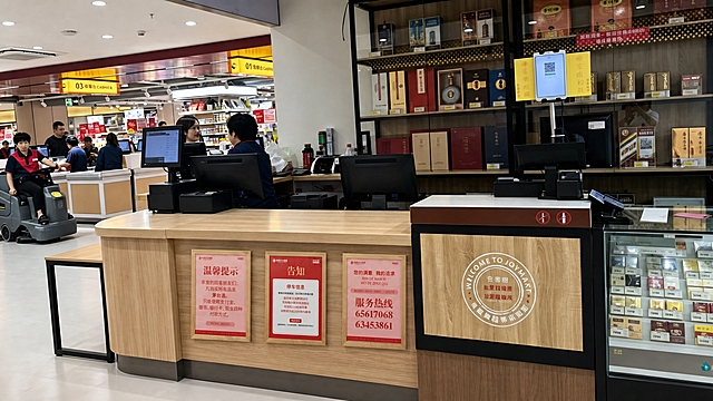 参考图1中三个告示牌在收银台立面上的摆放位置、透视角度和光影效果，将图3、图4、图5三个木框告示牌分别替换放置到图2超市收银台正面的木质立面上，从左到右依次为图4温馨提示牌、图3告知牌、图5服务热线牌。调整三个告示牌的透视角度、大小比例与图1中原牌一致，匹配图2场景的室内光照，添加自然的投影和环境反射，使告示牌完全融入图2的真实照片环境中，保持画面其他元素不变，整体真实自然，摄影级质感。