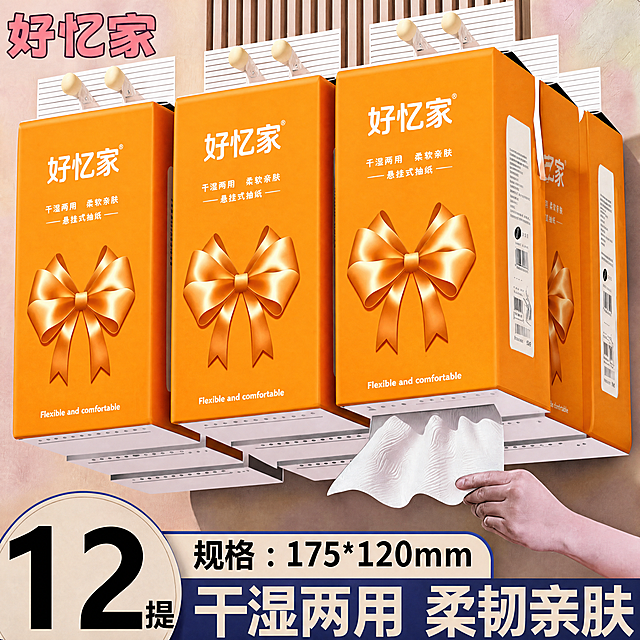 将白底图（图1）的外包装图案主题完全迁移到主图（图2）的多包盒装悬挂式面巾纸包装上：把每盒包装正面的原有红色福字圆形徽章、祥云花卉纹样和“心之泽”品牌信息全部替换为图1的亮橙色蝴蝶结礼物主题设计，包括整个包装正面鲜艳亮橙色背景、顶部居中白色大字“好忆家”和®、下方两行白字“干湿两用 柔软亲肤”和“—— 悬挂式抽纸 ——”、下半部分中央巨大的丝绸光泽感橙色立体蝴蝶结（带高光阴影）、底部白色小字“Flexible and comfortable”；保留图2多包盒装的形态、木质挂钩、木纹格栅墙、抽取纸巾的手、光线和整体尺寸完全不变，每包按透视贴合且蝴蝶结大小位置一致，文字清晰准确。
