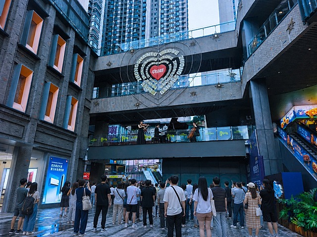 在地面广场区域增加一群正在观看演出的观众，观众姿态自然，有的站立有的驻足仰望舞台，穿着现代日常服装，人群分布合理，与场景透视和光线保持一致，整体画面真实自然，不改变原图其他元素