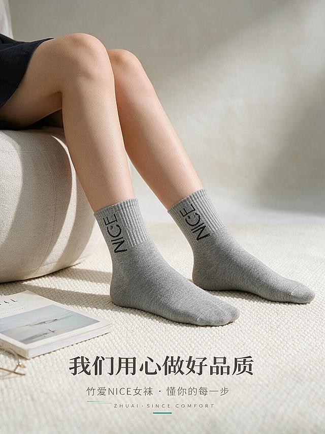[商品] 使用【图1】浅灰色竹爱NICE女袜中筒袜；商品处理：保留袜身"NICE"笑脸提花、袜型、浅灰色、针织纹理、中筒高度和罗纹袜口；自然理顺袜身，增强竹纤维针织纹理细腻感与柔软质感，不改变版型、颜色和结构。
[画面] 页面目标：场景氛围收尾页，强化日常通勤/居家舒适感与品牌品质承诺。画面主体为亚洲女性腿部穿着浅灰色NICE女袜，自然放松地搭在米白色布艺圆墩上，脚踩米白色编织地毯，旁边散落一本简约杂志和一副眼镜，营造慵懒舒适的居家/通勤准备场景。背景为浅米灰色渐变墙面，光线柔和温暖。产品占画面约45%，留有充足呼吸感。
[视觉] 套系策略：风格=简约高级日系商业摄影；标题字=现代无衬线粗体（思源黑体Heavy）；正文字=简洁无衬线体（思源黑体Regular）；主色=浅米灰+麻灰；背景延展=基于浅米灰做深浅层级、同色渐变和细腻织物/哑光墙面质感；强调色=竹青绿，仅用于小面积图标、引线和标签点缀；标题色=深炭灰；正文色=中暖灰；组件=极简文字排版、细线装饰、品牌感收尾；光影=左前侧柔和自然光，整体暖调通透，氛围温馨治愈。
[文字] 画面下方居中主标题"我们用心做好品质"，副标题小字"竹爱NICE女袜 · 懂你的每一步"，最下方一行极小字品牌感英文"ZHUAI · SINCE COMFORT"。文字全部横排，层级分明，收尾感强。
[规格] 图片比例3:4竖版（移动端详情页），分辨率1K，避免变形、错字、文字过小、冷蓝背景、袜子颜色改变、版型失真、低俗擦边、极限词、第三方平台Logo。