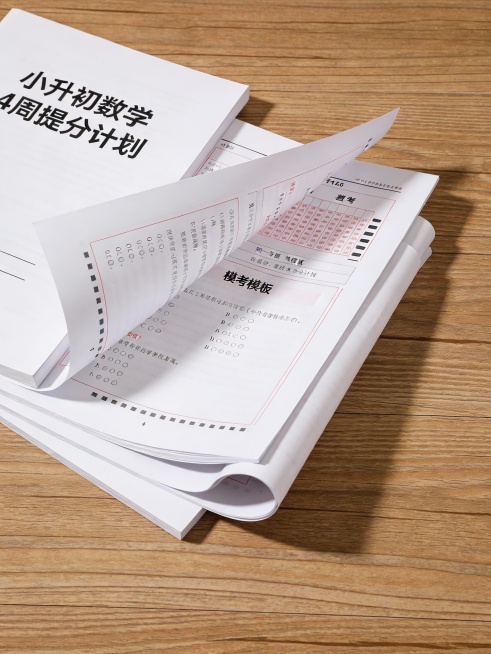 真实感桌面摆拍：几页A4打印纸摊开在木质书桌上，自然光照射。最上面是封面页，印有“小升初数学4周提分计划”；翻开的内页展示答题模板和模考卷局部。整体呈现“可直接使用的学习资料”质感，非电子截图。——比预览效果