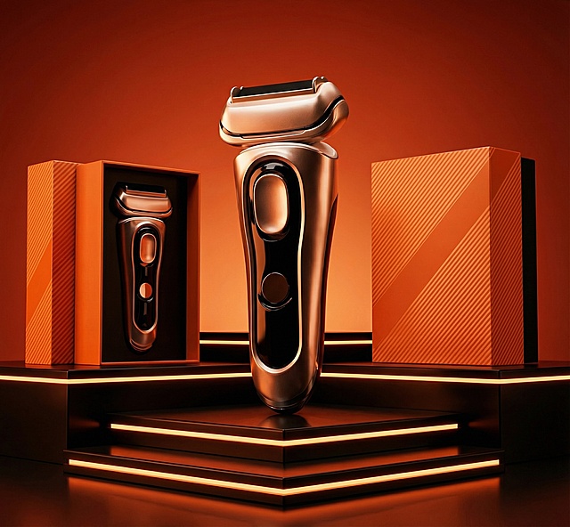 主体为电动剃须刀，搭配同产品的橙色斜纹包装盒，一个打开露出内部剃须刀，一个闭合。场景是带有橙色灯带的深色阶梯展示台，背景是渐变暖橙红色。风格为高端产品商业摄影，质感精致高级。色调以暖橙红与深黑为主，对比鲜明。构图为中心对称式，剃须刀位于前景视觉中心，包装盒分列后方两侧，低角度仰视凸显产品质感。细节上突出剃须刀的金属光泽、包装盒的纹理，灯光营造出奢华氛围感。