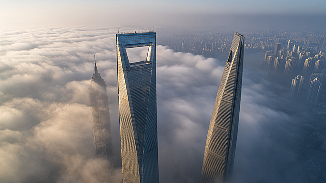 核心描述： 令人眩晕的垂直俯视上帝视角，特写镜头直视上海中心大厦顶部的V型螺旋缺口。
细节与构图： 右侧可见金茂大厦的塔尖，两座摩天大楼穿插在流动的云雾中。
光影与氛围： 白色的薄雾像丝绸一样在建筑间快速穿梭，柔和的体积光束斜射穿过雾气。低饱和度，冷灰色调，充满科技感和神秘感。
质感： 玻璃幕墙的冷硬质感，云雾的柔和质感，超高清，8k分辨率。