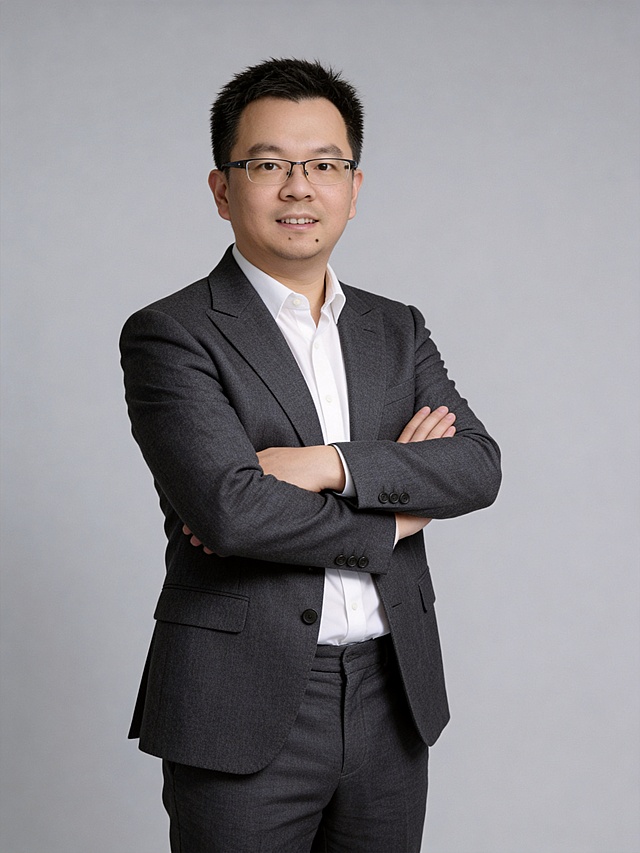 参考图中保留人物脸型、发型、年龄等特征生成职场形象照,标准焦段50mm,f/4光圈(f/2.8-f/4区间),平视视角(镜头与人物视线齐平);人物占画面70%,人物居中(居中构图),位于画面中心,为视觉聚焦点,入境范围头部及以下至臀部下方10cm(半身像);左右留少量背景空间;头部与画面顶部保留5%空间;头部发型完整,头肩比例协调,人物结构准确;发质微微柔顺，微微蓬松。身穿深灰色精纺羊毛混纺西装外套,(平驳领设计,面料呈细腻微微哑光质感);内搭白色高支精梳棉衬衫;下装深灰色精纺羊毛混纺西裤;着装正式干练;专业稳重;身形匀称,姿态端正,身体挺拔。呈双手抱胸的自然姿态，肢体放松且自信;保留佩戴眼镜，佩戴精致眼镜;简约微微中度灰色纯色背景(呈现均匀柔和质感),背景光线均匀柔和,强化色彩对比的高级感。极简干净;画质超高分辨率、细节清晰,现代精致感风格;肤质精细化处理;眼神直视镜头,目光坚定且澄澈,表情自然。嘴角上扬;肤质自然细腻,肤色健康均匀,皮肤状态清爽干净,保留真实皮肤细节｡正面柔光补光,4800K中性光,面部光比1:1.5｡中近景写实摄影,对焦清晰,面部雾面柔光,轻透裸肌感,高清保留皮肤细节｡分辨率4K,去除人物之外的所有元素。严格按照图片内容生成。画面比例3:4