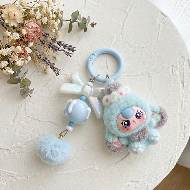 将这张毛绒挂件商品的背景换成奶油风ins风格，保持主体挂件商品结构和颜色完全不变，只更换背景。让商品居中放置，商品大小比例合适不要太小。背景为奶白色肌理感桌面，左上角点缀干燥花装饰，柔和自然光，光影温柔干净，画面干净简约，凸显商品。保持商品原样，不要修改商品本身。