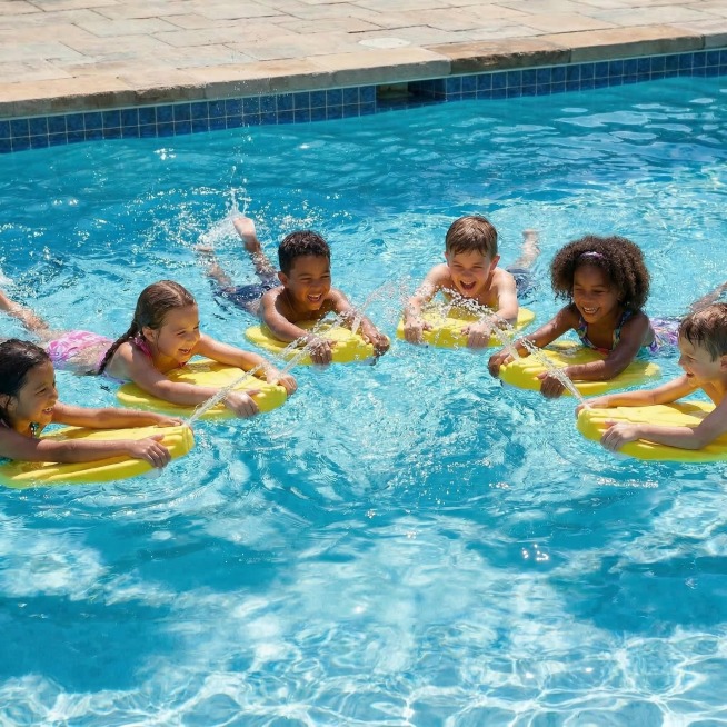 去除图中顶部黑底区域及文案“SPLASH FUN & LEARN - ULTIMATE WATER JETS”，其余内容完全保留：多名儿童在清澈蓝色泳池中使用黄色喷水浮板戏水，水面有水花与波光，阳光充预览效果