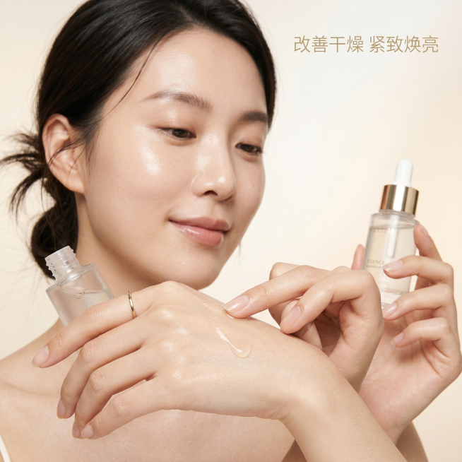 [主图4 护肤功效展示] 亚洲女性模特（同一位保持风格统一）手背涂抹精华的特写，展示产品使用过程，模特皮肤水润透亮，表情自然享受；背景为简约浅香槟渐变柔光，文字标注"改善干燥 紧致焕亮"，浅金色小号无预览效果