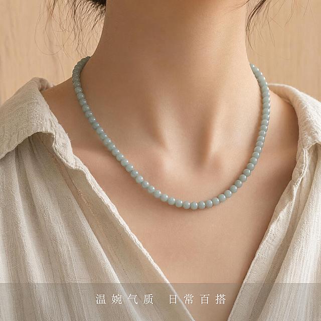 [主图-4] 且末蓝和田玉珠链佩戴效果展示，气质国风局部模特图。氛围风格：日常佩戴氛围感，温婉雅致。画质：商业人像珠宝摄影，质感柔和高级。元素：选用年轻东方女性模特，穿简约素色棉麻衬衫，展示珠链佩戴于颈间的效果，保持珠链颜色、大小、整体造型与原图完全一致，珠子圆润色泽均匀，无变形色差。模特仅展示颈部到锁骨区域，面部不进入画面，突出珠链主体。背景为浅原木色调墙面，简洁干净。商品主体珠链占比约65%。光影：柔和窗边自然光，温润通透，突出玉石哑光质感，光影自然。配色：素色米调服饰与浅木背景，突出且末蓝珠链本身颜色。视角构图：平视锁骨局部特写，景深自然。文字版式：底部轻浅半透明条，居中短句“温婉气质 日常百搭”，白色小字，不抢主体。比例分辨率：1:1 比例，2K分辨率，文字清晰，超高清。负向提示词：变形，文字错乱，产品模糊，背景杂乱，水印，电商平台Logo，模特面部入镜，色彩失真。