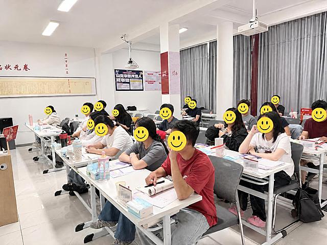 给图片中所有桌牌上的姓名文字部分打上马赛克模糊处理，包括刘瀚博、钱嘉彤、杨长青等所有桌牌上的名字，只模糊名字文字区域，保持桌牌其他部分、人物、教室场景和所有物品不变，马赛克效果自然