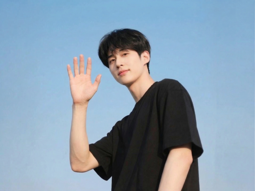 将图中男生原本放在额头旁的手势修改为挥手打招呼的姿势，保持人物其他特征、穿着和蓝天背景不变，自然真实预览效果