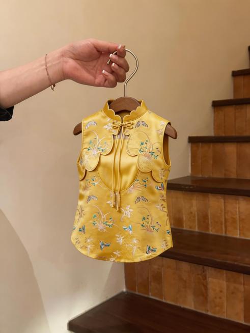 将图中衣架上的龙纹旗袍替换为新生成的黄色中式无袖宠物服装，保留衣架、手部、楼梯背景不变，服装使用指定的蝴蝶花草刺绣面料，还原花瓣领口和盘扣细节预览效果