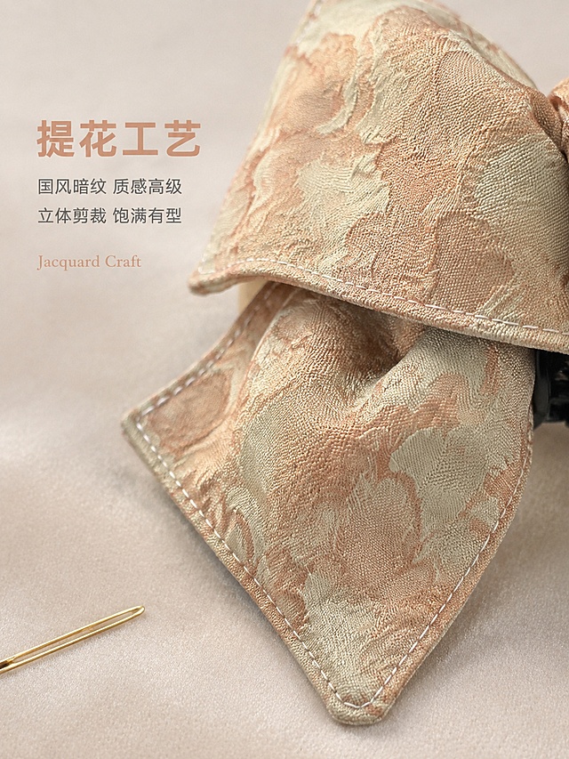 重新生成新中式提花蝴蝶结抓夹工艺细节图。严格以实物图颜色为准：底色浅米偏淡绿调，提花纹理淡橘粉色带金闪，整体颜色浅淡柔和。微距特写聚焦蝴蝶结一角的提花面料纹理和缝线细节，提花暗纹花卉精致，面料有微微光泽感，缝线工整细密。背景为浅香槟色丝绒材质，左下角放一根细小的金色缝纫针做参照。左侧文案：主标题"提花工艺"淡橘粉色大号粗体，下方两行小字"国风暗纹 质感高级""立体剪裁 饱满有型"浅灰色中号，底部小字英文"Jacquard Craft"。产品占比约70%，平视微距视角，景深较浅。顶部柔光均匀打光，提花纹理有明暗层次。颜色必须与实物图完全一致，杜绝偏深。3:4竖版。
