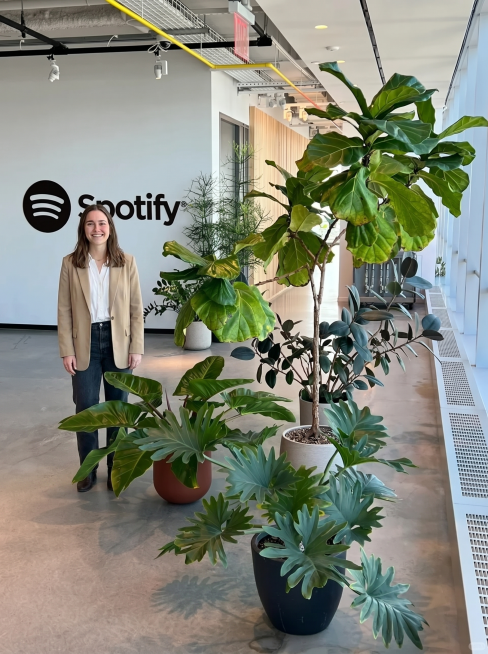 在这张Spotify办公室绿植照片上增加一个年轻女生，女生面对镜头微笑，表情自然，保留原来所有绿植和场景预览效果