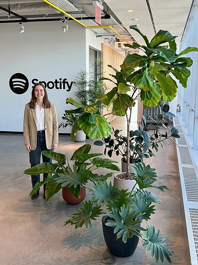 在这张Spotify办公室绿植照片上增加一个年轻女生，女生面对镜头微笑，表情自然，保留原来所有绿植和场景