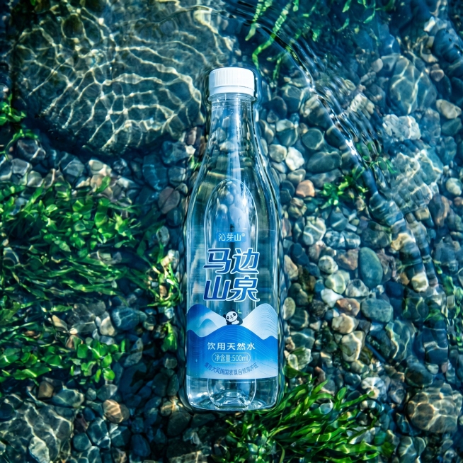 马边山泉饮用天然水，瓶子竖直站立在清澈见底的浅滩中，溪水刚好没过瓶底，周围是细小鹅卵石和水草，阳光从水面直射下来形成迷人光斑，突出矿泉水的纯净冰爽感。不需要显示任何文案。保持瓶子外观（物理结构、材质质预览效果