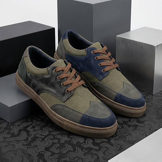 生成一双男士帆布鞋，鞋子整体是拼色设计，搭配不同材质。其中某一处使用图片提供的黑色皮革，带有黑色皮革纹路，颜色符合男士沉稳风格。鞋子放置在黑色皮革材质上方，背景是简洁的电商几何场景，整体风格商业产品图，高清质感