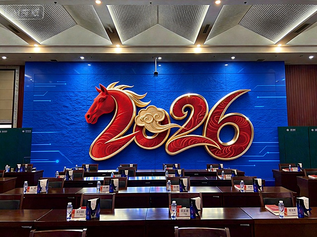 在会议室原图的背景墙上改成科技蓝文化墙，将图2的2026红色金马艺术字放在文化墙居中位置，做一个整体造型，保持会议室前方桌椅不变