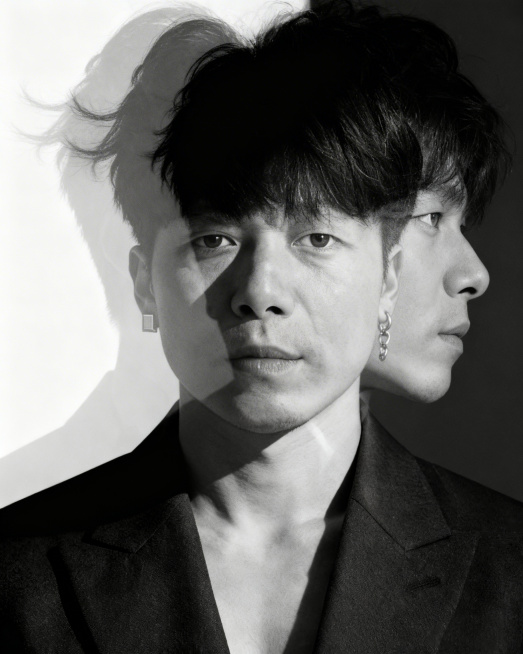 图中人物五官不变，年轻东亚男性（18-25岁）的双重曝光黑白写真，近景构图。前景是他正面朝向镜头，眼神锐利直视，神情冷峻；头部与发丝处叠加半透明的侧影（侧颜向右凝视），形成虚实交织的视觉效果。身着黑色预览效果