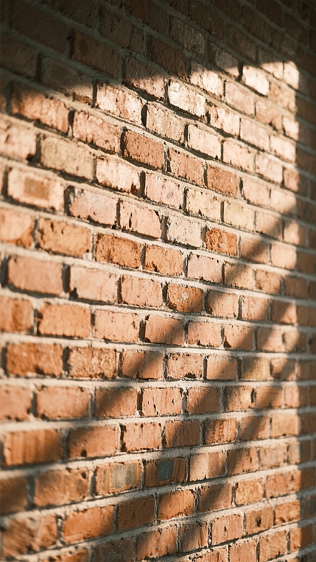 一面由大小均匀的红褐色砖块砌成的墙面，砖块之间的灰白色 mortar 线条清晰可见，部分砖块边缘带有自然的磨损和色泽深浅变化，墙面整体呈现出质朴而略带粗糙的质感。墙面上投射着柔和而温暖的午后阳光，光线从左侧斜上方照射下来，在砖块表面形成深浅不一的光影交错效果，营造出一种宁静而温馨的氛围。