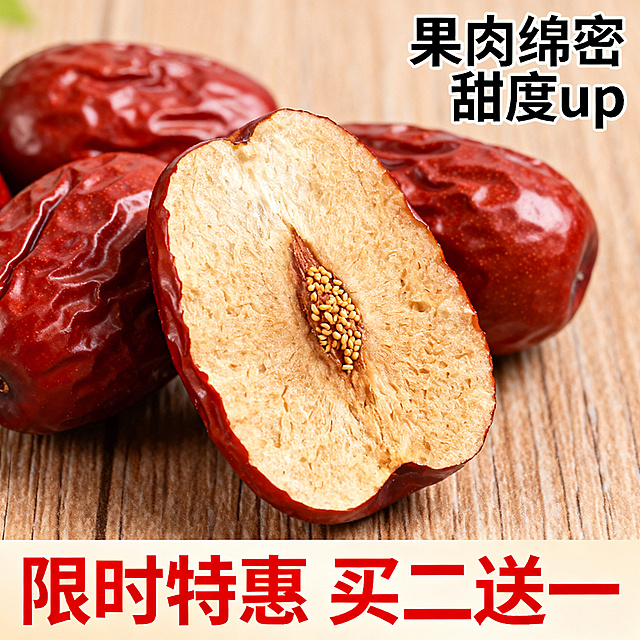电商主图，切开的红枣展示出厚实果肉和细小枣核，旁边摆放完整红枣，背景是浅棕色木纹桌面，右上角标注"果肉绵密 甜度up"，底部用红色醒目字体写"限时特惠 买二送一"，视觉聚焦产品细节与促销信息