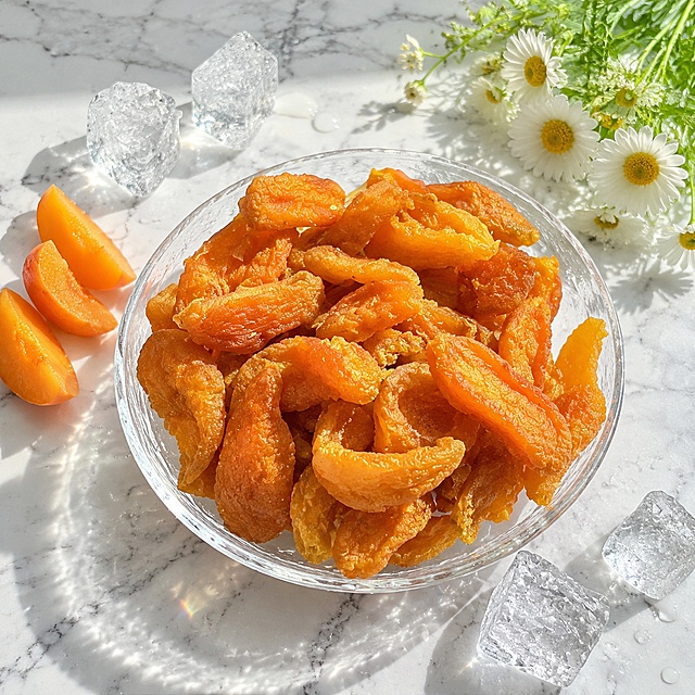 超写实食品摄影。
主体：杏干（果脯）严格参照上传产品图，完整保留所有可见的形状、纹理、颜色、质感与果肉纤维结构，与上传图完全一致；自然融入场景光影，与场景共处同一物理空间。产品占画面约60%，完整不裁切，背景无其他同类食品包装。
构图：45度俯拍，居中构图。
风格：清爽夏日风。
场景：清凉夏日桌面场景，阳光明媚。
承载：①中央，一块白色大理石台面，纹理自然；②台面上，一个透明玻璃碗，碗中堆放着杏干。
陪衬物：①玻璃碗旁，几块晶莹剔透的冰块，表面有水珠凝结；②碗的左侧，几片新鲜杏瓣，果肉饱满；③碗的右侧，一小束白色小雏菊，清新点缀。
动态生机：冰块表面水珠滚落，果脯表面泛着清凉的光泽，整体清爽诱人。
配色 / 材质：橙黄 / 冰白 / 大理石灰 / 嫩绿；果脯胶质 / 玻璃 / 冰 / 大理石。
光影：明亮清爽的自然光从正上方洒下，果脯表面高光清透，冰块折射出彩虹光斑，整体明亮干净，夏日清凉感十足。
参数：4K 写实光追。严格锁定宽高比为 1:1。