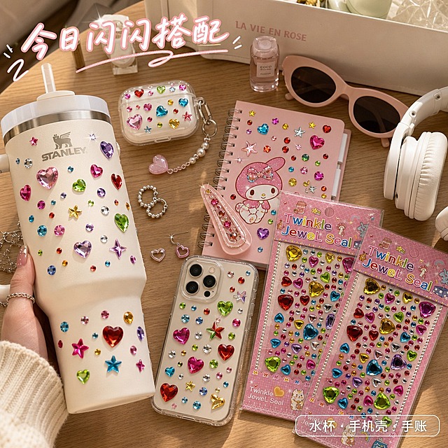 第5张 多场景应用主图｜加州少女DIY桌面
1:1正方形商品主图，加州阳光美式ins风，暖调自然光+补光，浅木色桌面，整体松弛生活化，种草感强。
画面桌面随性摆放日常物件：白色大容量冰霸杯、透明手机壳、粉色手账本、发夹、耳机壳，物件表面均粘贴同款彩色钻石贴纸，贴纸贴合平整，钻面高亮通透，切面反光自然，与包装钻面质感完全统一，真实呈现DIY装饰效果。画面右下角错落摆放两款原图钻石贴纸包装，作为产品露出，占比适中不抢场景主体。桌面点缀银色耳环、粉色甲油瓶、复古墨镜、白色耳机等美式少女小物，构图松散随性，像真实桌面分享。可局部露出少女手部拿取水杯，增加真实感。
画面顶部偏左用手写感标题标注「今日闪闪搭配」，白字浅粉描边；右下角配迷你标签「水杯·手机壳·手账」，透明底白字，融入场景不突兀。