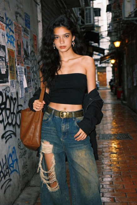 法国女生，一位超高颜值的黄皮法国女生，长相小众，个性十足，黑色大波浪自然垂落，表情慵懒随性。穿搭为黑色抹胸露脐上衣，搭配做旧水洗蓝阔腿牛仔裤（裤侧有大面积磨白破洞设计），腰间系一条带有金属扣的复古腰带预览效果