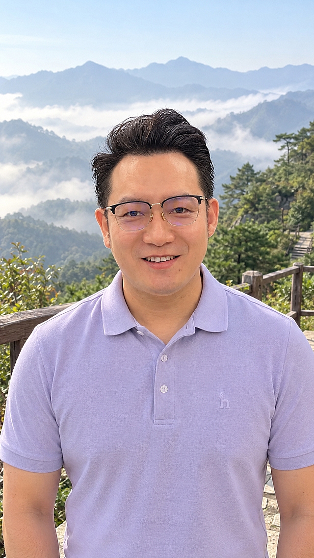 以参考图中人物的面部、五官比例与微笑表情为严格依据，生成一张真实生活照，竖版9:16。

人物一致性（最高优先级）：严格复制参考图的自然微笑表情（眼睛自然睁开、眼神带笑意、轻松露齿浅笑）、脸型偏圆润饱满、眉眼形状与间距、鼻型、嘴型、下颌线与颈部厚度、肤色与年龄感；保留细边半框眼镜；发型与参考图一致（头顶稍长向后上方蓬松、两侧较短、露出额头）。不瘦脸、不美白磨皮、不网红化。

服装：浅紫色短袖polo衫，经典三粒扣款式——下面两粒扣子扣好，最上面一粒扣子解开；质地真实、版型合身。

场景：山间徒步观景平台，背景为晨雾缭绕的青山与树林、登山步道，清爽的山间日光，人物自然站立微笑看向镜头。

质感与光线：真实自然的户外日光，面部光影均匀；真实手机拍摄感，胸像到半身、头部大小适中；皮肤干净真实有质感（不过度磨皮），高清细腻4K，无文字无水印。