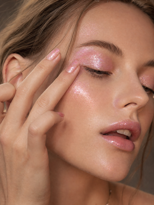 极致特写美妆大片，年轻欧美女性，用指尖轻轻涂抹浅粉色超闪闪粉液体状眼影，面部表情柔和，微张的嘴唇，皮肤清透带有光泽感，颧骨和嘴唇上也薄薄涂了一层浅粉色超闪闪粉液体状眼影，粉色精致美甲，温暖柔和的影棚灯预览效果