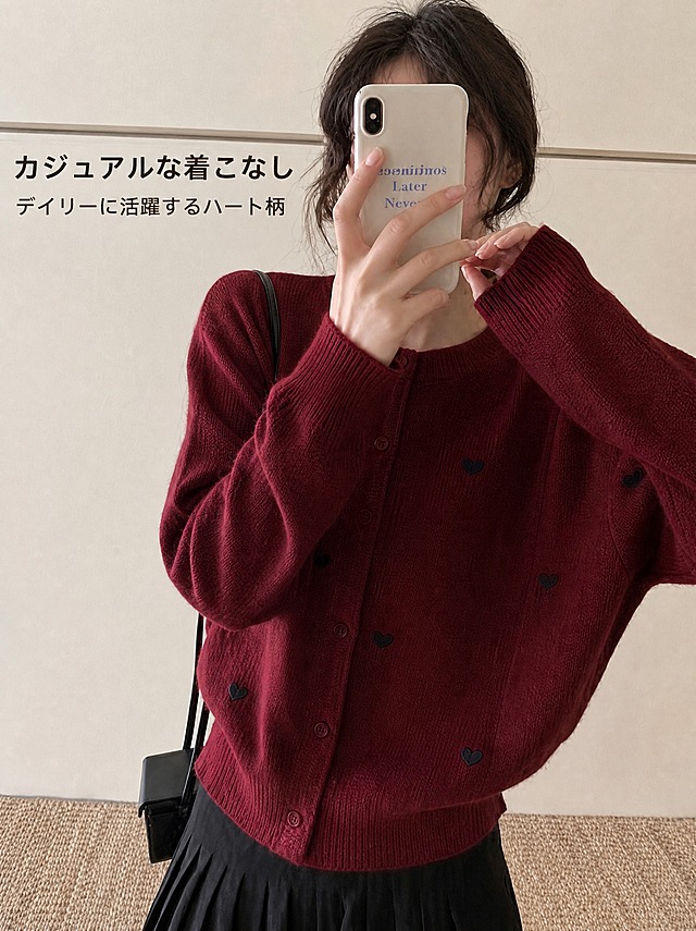 以这张图为原图进行编辑：严格保持画面中的人物、手、手机、服装（酒红色爱心印花针织开衫）、下装、背景、构图、光影与整体色调完全不变，不改变商品的颜色、款式、结构、纽扣与爱心图案位置，不改变人物姿态。只做两件事：(1) 把图片提升为更高分辨率，画面更清晰锐利、针织质感与细节更丰富；(2) 在画面空白负空间（左上角或下方留白处）添加日语卖点文字，主标题“カジュアルな着こなし”，副标题“デイリーに活躍するハート柄”，横排、现代无衬线日文字体、与背景形成强对比、清晰可读、不遮挡人物与商品。不要新增其他文字、水印、Logo 或装饰。输出 3:4 竖版高分辨率图。