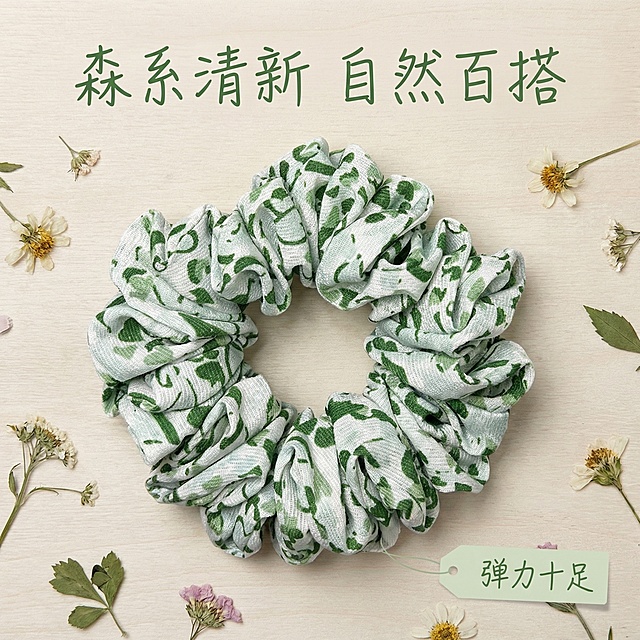 基于原图的碎花大肠发圈，仅展示绿色款发圈单品，保留产品外观与原图一致。背景为浅米黄色木纹高质感背景，搭配清新小碎花点缀，整体风格清新高级。添加文案 "森系清新 自然百搭"，右下角浅色标签 "弹力十足"，字体为清新手写体，颜色从产品提取，排版简约，不遮挡产品主体，光影柔和，符合拼多多电商主图风格