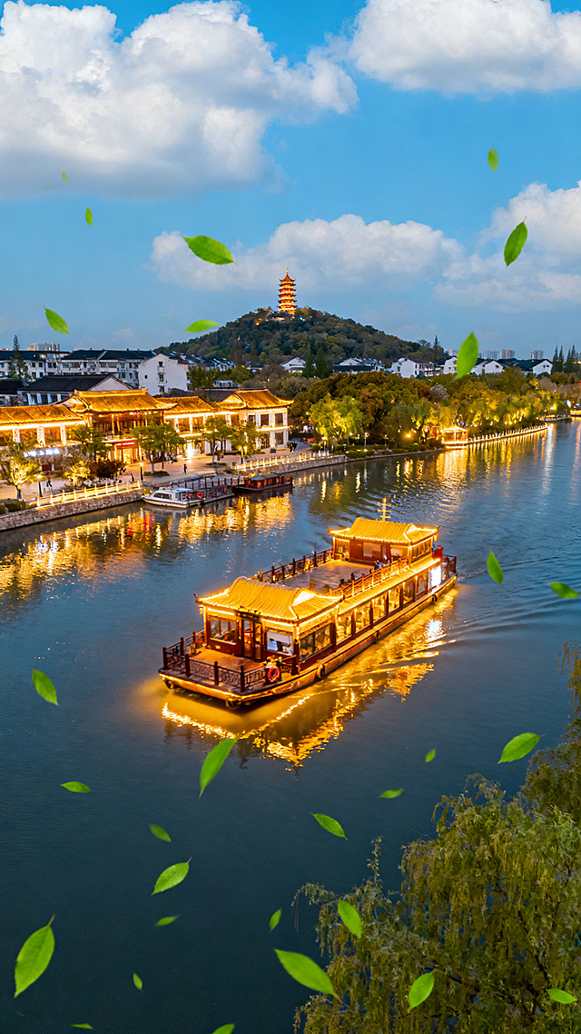 俯视图夜景，南通濠河灯火通明，游船为主体，远景狼山清晰可见，蓝天白云春意融融，河面绿叶轻飘，场景唯美灵动