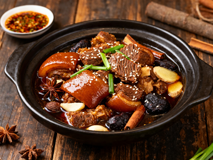 药膳美食何首乌焖羊肉，带皮羊肉焖至Q弹软嫩，表皮呈诱人的深琥珀色，吸收了何首乌的药香，搭配八角、桂皮、姜片等香料，汤汁浓郁挂汁，撒上一小撮白芝麻和青蒜叶提香，盛放在铸铁深盘中，摆放在复古木质桌面上，旁预览效果