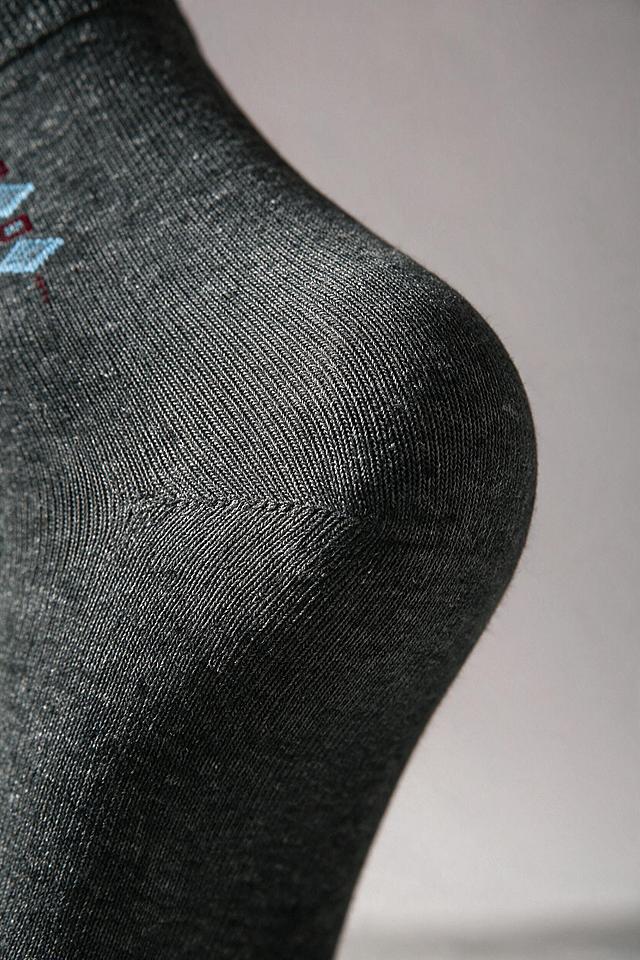 参考图2的特写构图和高级光影风格，基于图1的深灰色袜子制作袜跟细节特写海报，聚焦袜跟部位放大展示，100%继承原袜子的针织面料、纱线纹理、织物颗粒、原有印花、褶皱、明暗光影，袜子质感完全复刻原图，禁止重新生成袜子材质，袜跟的Y型缝合结构和针织纹路清晰可见，仅适配环境光影为柔和侧光效果，袜子本身纹路细节不做美化、不抹平颗粒，不要塑料光滑感，真实实拍纪实质感，不过度修图，画面干净无任何文案，背景为柔和的浅灰色调虚化背景