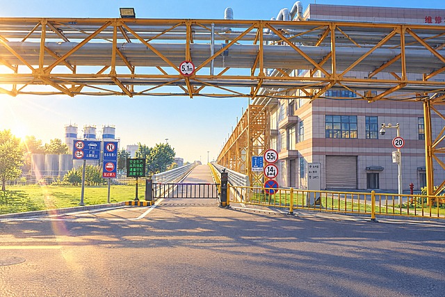 将这张工厂入口道路的照片转换为日系动漫风格，保留画面中的管道桥架、道路、栏杆、交通标识和建筑的整体构图与结构，整体呈现五六月份清晨的氛围，柔和的晨光，清新通透的空气感，天空干净无云，色调清新明亮，动漫插画质感，细腻的光影，画面干净整洁