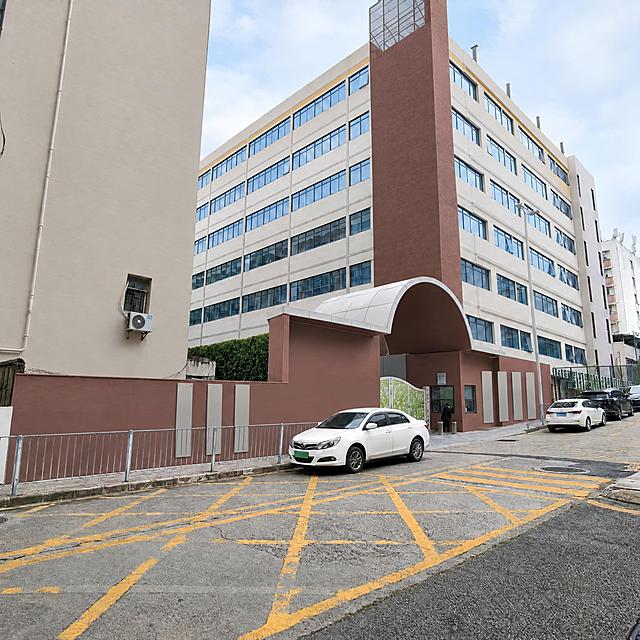 保留原照片的街景构图、透视与地面黄色网格标线，只重新调整建筑与墙面配色：校门竖向塔楼由浓烈酒红改为灰调红棕／深砖赭色，只保留一条竖向色带，其余相邻墙面统一为暖米灰；左侧米黄建筑也统一为暖米灰；建筑立面原有的黄色饰条降饱和为浅芥末黄窄线条；拱门与红色矮墙降饱和为灰调红棕；招牌位置保留但不出现文字。整体低饱和、通透、年轻、国际化简约。画面中不出现任何文字、字母、数字、标语、校名、logo。