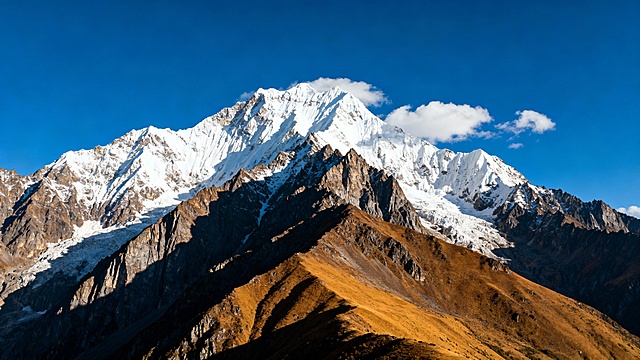 壮丽的雪山全景摄影，雄伟的山峰群在清澈的深蓝色天空下巍峨耸立，山顶覆盖着洁白厚实的积雪，山体岩石呈现出深褐色与灰色的自然纹理，阳光从侧上方照射，在山峰表面形成明亮的高光与深邃的阴影对比，勾勒出尖锐的山脊和陡峭的岩壁轮廓，几朵形态轻盈的白云点缀在山峰之间的蓝天中，近处的山峦呈现出温暖的棕黄色调，整体画面气势恢宏、细节丰富，具有极高的写实感和自然光影层次，营造出宁静而壮阔的高山氛围。