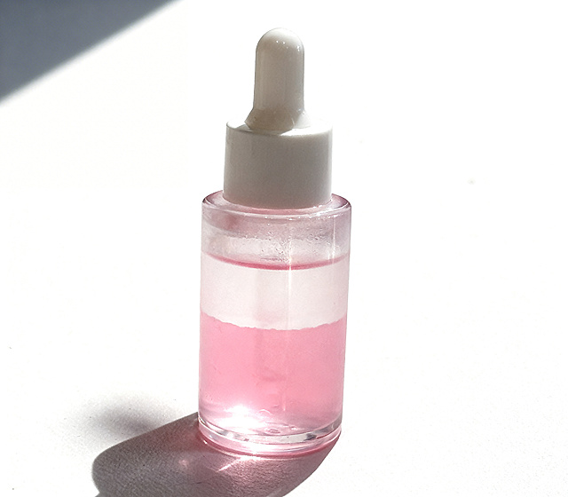 不改变产品原有颜色，对这瓶精华液进行商业级精修，去除表面瑕疵和划痕，增强光影立体感，强化材质明暗关系，提升整体质感与高级感，提高整体画面亮度，保留原有构图和视角，高折射率玻璃材质，通透体积光，通透无杂质，超清画质，智能降噪，细节锐化，8k分辨率，商业棚拍光，体积光，柔和阴影，纯白背景，真实接触阴影，修复表面划痕，材质抛光，崭新干净，保留原产品粉色分层色调
