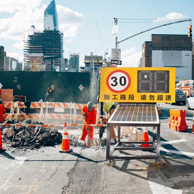 将抠好的施工路段测速警示标识放置到城市道路施工场景图的前方路边合适位置，自然融入画面，保持真实感预览效果