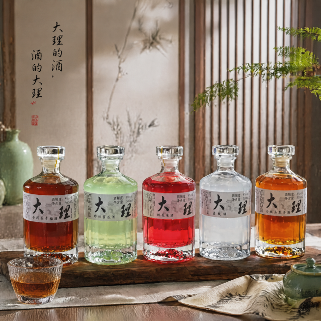 修改图片：将左上角原有的文案“大理的酒”替换为“大理的酒，酒的大理”，文案改为黑色手写细书法字，排版为竖排，呈现一高一低的错落效果，要求字体柔和不抢眼，保持整体高级感；将前景的玻璃酒杯中添加红棕色酒液预览效果