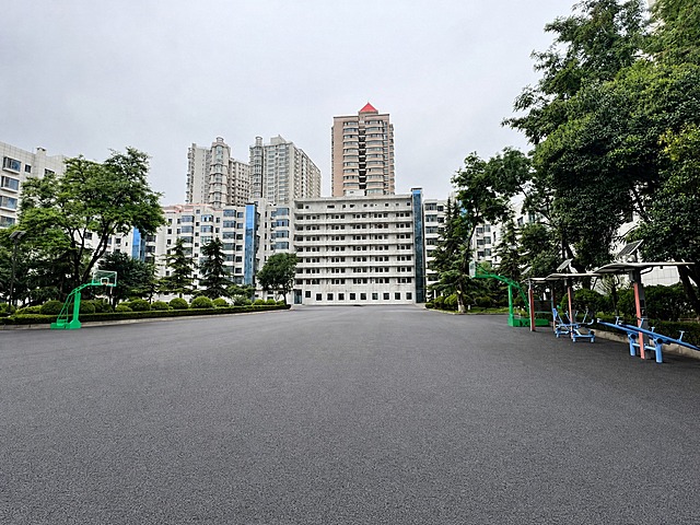 去除画面中所有的人物和所有的汽车，去除地面上的水渍，使地面变为干燥平整的沥青路面，保持其余景物（建筑、树木、篮球架、健身器材、天空等）不变，画面自然真实，光影协调，无修图痕迹