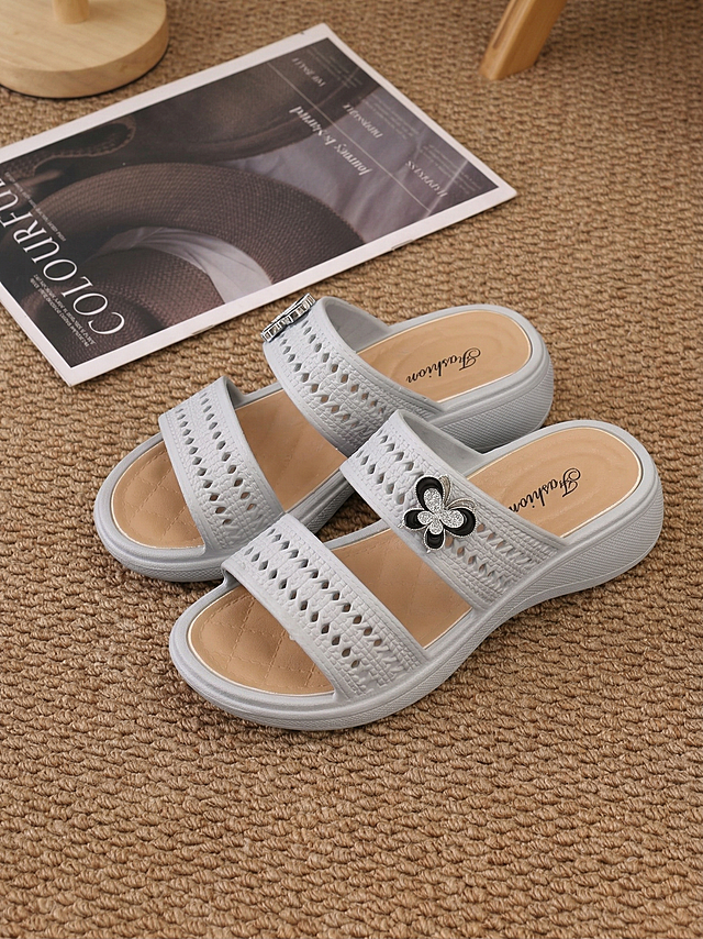 将图片中米黄色的凉拖更换为第二张参考图中鞋子的浅灰色，保留鞋子原有的镂空纹理、蝴蝶装饰、浅棕色内底、整体造型以及周围的地毯、杂志等场景细节不变