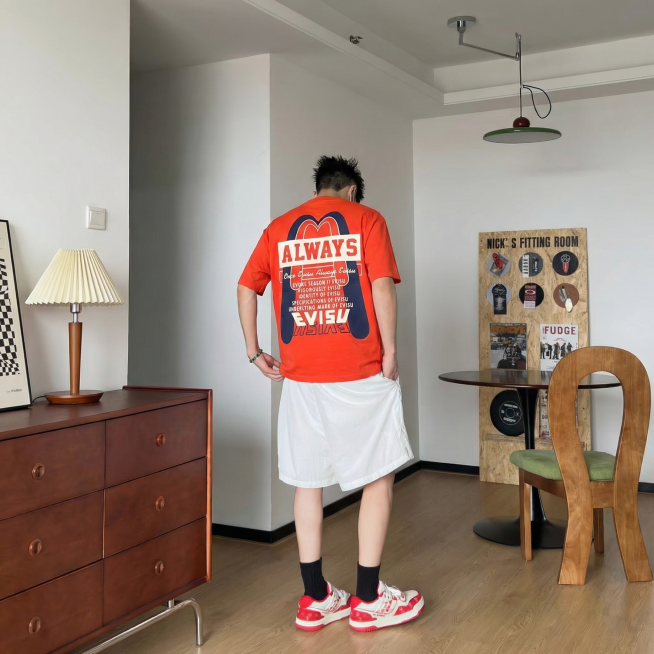 将图中模特身上的红色T恤替换为第二张图里带有ALWAYS和EVISU图案的橙色T恤，保持模特姿势、场景、光线和其他衣物不变，自然真实不违和预览效果