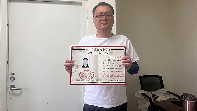 请将参考图1的【四川省普通高中会考毕业证书（红色封皮翻开状态）】1:1 还原其形态、文字、印章、黑白照片、红色封皮、细节纹理、污渍质感等所有细节，替换掉参考图2模特手中的白纸，保持参考图2中双手持握的姿势、手指位置、抓握角度完全不变；完全保持参考图2模特的身姿、面部、发型、眼镜、气质、动作/姿态不变（含手部位置、朝向、重心、肩线）；模特身上参考图1未覆盖的部位（白色T恤、黑色裤子、左臂深色袖套）严格保持参考图2原样；画面背景（白色门、办公椅、桌子、暖水壶、墙面）、光影、构图、景别严格保持参考图2原样，不做改写。

参考图1的毕业证书1:1还原所有细节；尺寸贴合双手持握比例，证书正面朝向镜头，自然展开，角度和透视与参考图2中原白纸完全一致。

超写实高清画质，细节层次丰富，色彩还原真实，整体质感自然真实；商业摄影写实质感。

毕业证书持握位置合理；双手与证书自然接触，手指抓握证书边缘姿态自然；入画部位人体结构正确（手指数量正确、关节自然、手腕线条柔和）；证书与手部接触处有自然接触阴影与压痕；证书与人体边界清晰可分、层次分明、接触点自然贴合。
