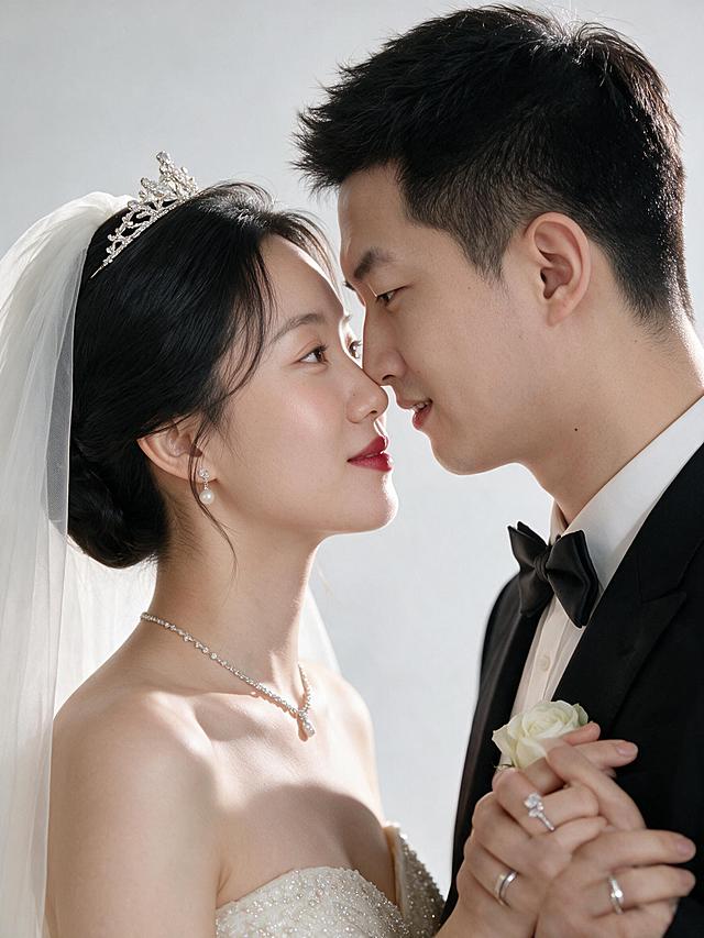 超高清现代中式婚纱摄影作品，干净简约、高级质感、柔和暖白色调。纯净浅灰白色影棚背景，柔和均匀的影棚专业布光，人物面部明亮通透，侧光营造立体感，肤质细腻有光泽。整体暖白色调，画面明亮干净，肤色白皙通透自然红润，婚纱呈现象牙白质感。超高清画质，保留皮肤细腻纹理、婚纱珠片刺绣细节、面料光泽质感，背景柔和虚化，人物清晰锐利。

人物：严格使用上传的三张参考肖像中的同一对新人，男性为唯一新郎，女性为唯一新娘，100%沿用原图五官、脸型、肤色，禁止修改，面部特征精准还原，表情自然真实。男性身高约178cm身形挺拔修长，女性身形纤细优雅，双人同框时男性高于女性10-12cm，比例协调自然。

新娘造型：黑色长发，韩式优雅低盘发，留有柔和碎发丝修饰脸型；头戴精致水钻皇冠，搭配轻薄白色头纱；清透裸肌妆容，自然柔和眉形，淡粉色腮红，气质正红色唇妆，妆感干净高级；象牙白抹胸婚纱，通体点缀细密珠片刺绣，面料有光泽质感，裙摆蓬松优雅；佩戴水钻项链、珍珠耳饰、钻石戒指；整体端庄大气、温婉优雅。
新郎造型：黑色短发，干净利落的纹理感造型露出额头；自然清爽妆容肤色均匀；黑色修身礼服西装套装，白色衬衫，黑色领结，黑色皮鞋，胸口佩戴白色玫瑰胸花；佩戴银色婚戒；整体儒雅绅士、挺拔俊朗。

第6张动作：额头相触。新人额头轻轻相触，鼻尖相对，微睁眼，表情温馨幸福。胸部以上近景特写，背景柔和虚化，氛围浪漫细腻。

禁止：复杂花哨背景、暗沉灰暗色调、过度磨皮、手指变形、五官比例失调、表情僵硬、服装款式更改、画面杂乱、人物比例失调