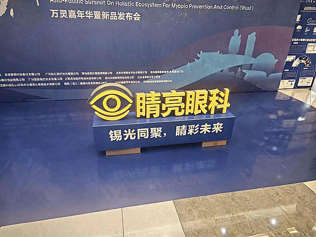 将展示台上的logo完全替换为第二张图片中的睛亮眼科logo，保持原来的黄色立体效果，保留logo的图形和文字样式，背景和展示台保持不变