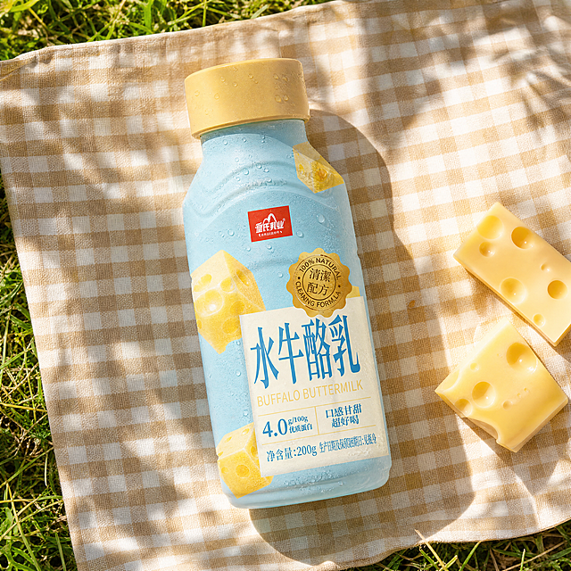 高品质产品摄影，户外野餐场景
主体：水牛酪乳瓶装饮品严格参照上传产品图，完整保留瓶身轮廓、结构、比例、材质、颜色与瓶身所有文字信息。产品为画面唯一主体，放置在野餐布中央，背景无同类饮品包装。
构图：45度俯拍构图，产品完整不裁切
风格：清新自然
场景：户外草坪野餐，明媚阳光下，格纹餐布
陪衬：①浅米色格纹野餐布，②细碎阳光树影落在餐布上，③旁边散落一两块新鲜奶酪块，④瓶身外壁覆着冷凝小水珠
配色/材质：浅蓝/米白/暖黄/草绿，纯棉格纹/新鲜奶酪/青草
光影：午后自然窗光从斜前方45°照射，清透明亮，突出瓶身水珠质感和奶酪的奶黄色泽，整体暖调清新，无灰暗阴影
严格锁定宽高比为 1:1