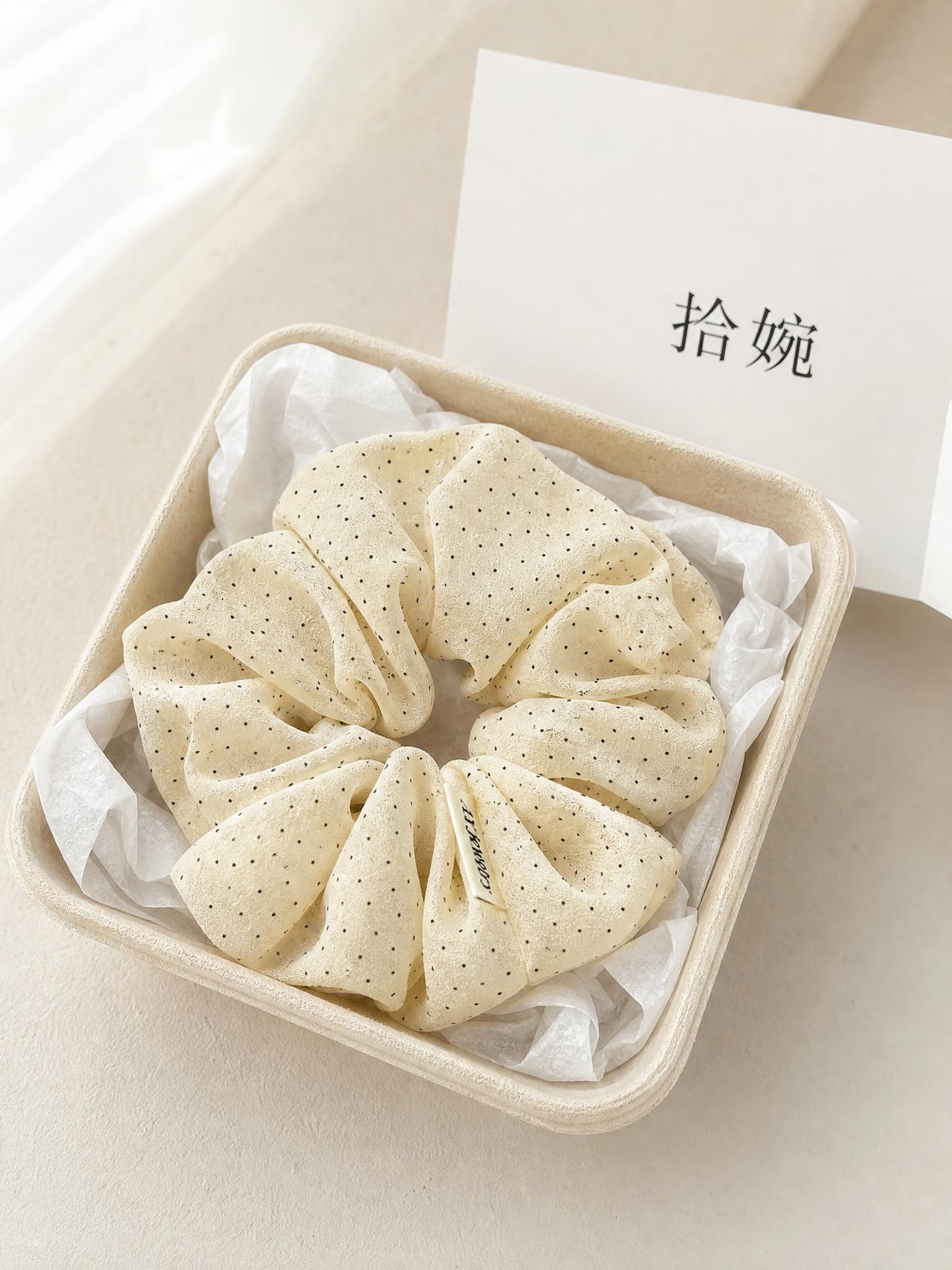 俯拍平铺静物摄影，韩系黑白小波点雪纺大肠发圈放置在米黄色可降解… - 图片创意预览