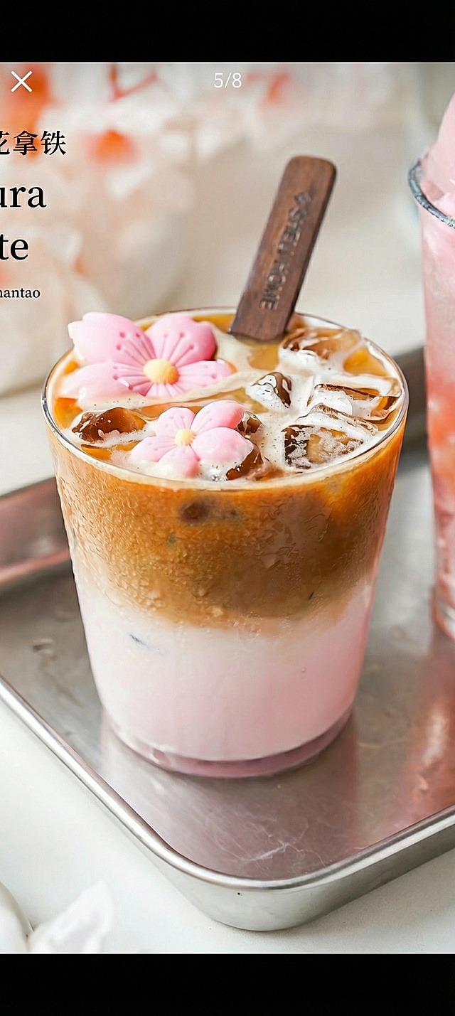 生成图中的樱花拿铁咖啡，分层的粉色基底和棕色咖啡层，顶部有冰块、粉色樱花装饰和木质搅拌棒，放置在金属托盘上